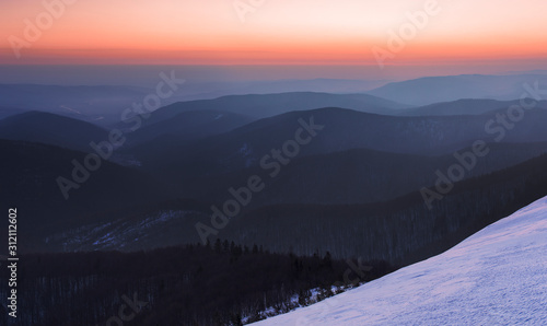 Winter Carpathians. Morning twilight on mountain ridges covered with deciduous forest with orange sky on the horizon. Morning twilight in the winter Carpathians. Beskidy area.