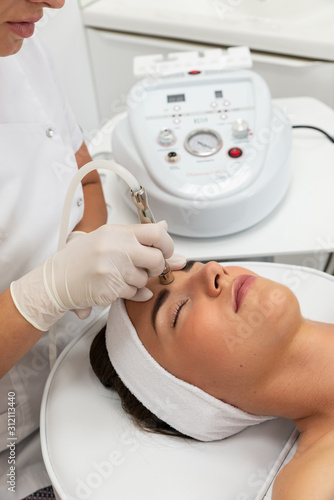 Kosmetolog wykonuje zabieg mikrodermabrazji skóry twarzy kobiety w salonie kosmetycznym. Kosmetologia i profesjonalna pielęgnacja skóry. Medycyna estetyczna