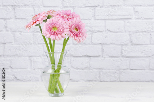 Bouquet of pink Gerber daisy flowers in a clear vase isolated on an elegant white fabric draped background