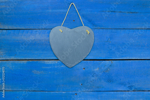 Blank slate heart sign hanging by rope on antique rustic blue wood door; Valentines Day holiday and love concept background with painted copy space