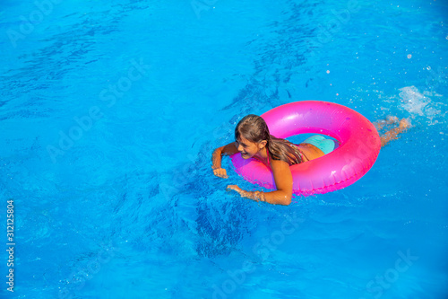 Pretty teen girl in swimsuit playing with pink inflatable lifebuoy in swimming pool on vacation.