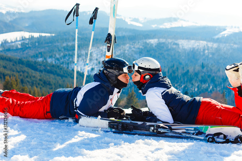 Young happy couple lying in snowy mountains with cross ski