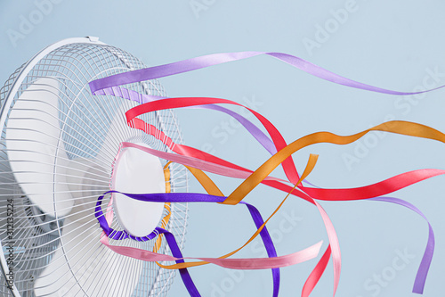 Foto Electric fan with fluttering ribbons on color background