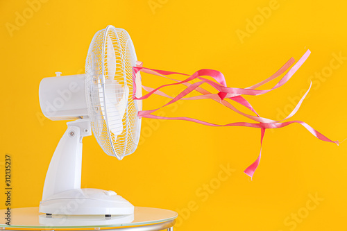 Electric fan with fluttering ribbons on color background photo