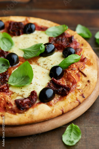 Pizza with mozzarella cheese, marinated tomatoes, black olives and fresh basil. Brown wooden background. 