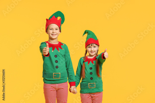 Little children in costume of elf showing thumb-up gesture on color background