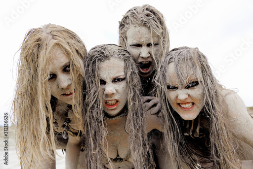 A group of four women's faces are covered with mud  and dirt.Their hair is tangled in a mess. The facial  expression shows them to be unattractive and filthy.