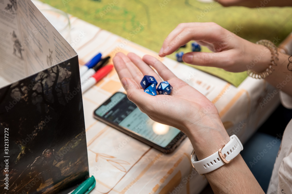 Girl playing dices for the role game dungeons and dragons, using the smart phone for play.