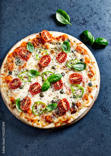 Pizza with cherry tomatoes, mozzarella cheese, jalapeno pepper, capers and fresh basil. Dark stone background. Top view.