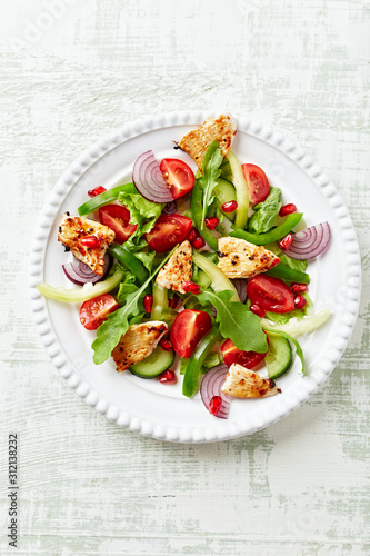 Healthy Salad with Pomegranate seeds, Chicken Briest, Green Pepper and fresh Basil. Bright wooden background. Top view. Copy space.