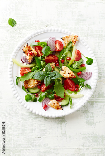 Healthy Salad with Pomegranate seeds, Chicken Briest, Green Pepper and fresh Basil. Bright wooden background. Top view. Copy space. 