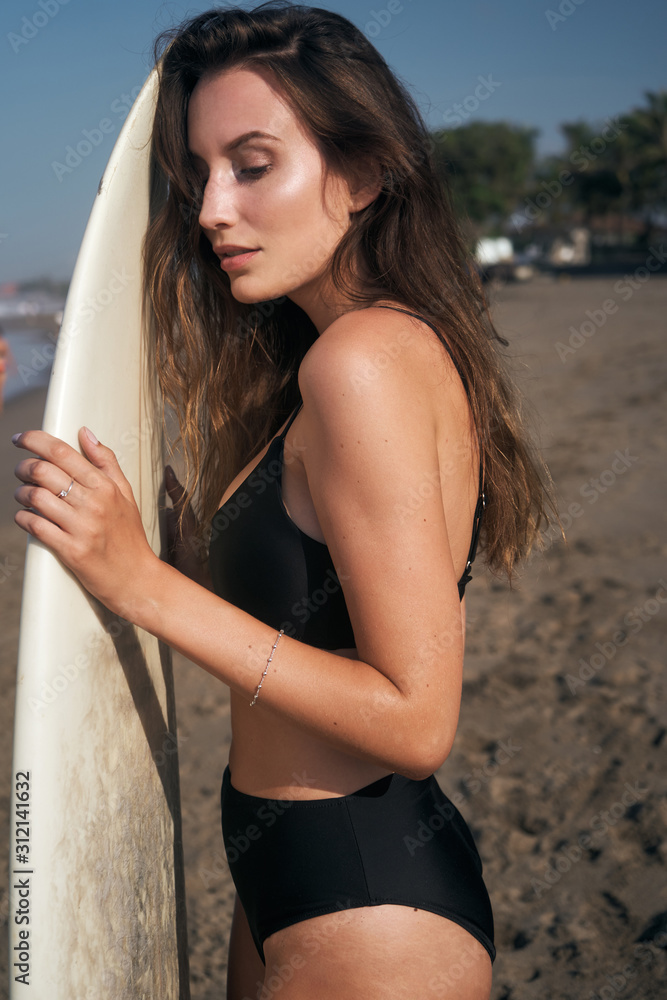 Female model with long hear style and beach wear with surfboard at sunny morning at the Balinese ocean beach Female model with long hear style and beach wear with surfboard at sunny morning at the Balinese ocean beach