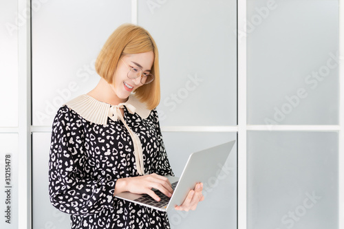 smart asian female stand and holding laptop with hand in office, she search information and play internet with wireless, communication technology