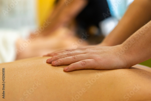 A close up shot on the hands of a Swedish massage student rubbing the back of a caucasian person, with blurry background and copy space to top
