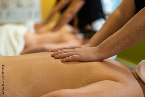 Students practice effleurage rubbing techniques in the classroom, hands of a pupil are seen on the back of a volunteer during exam preparation