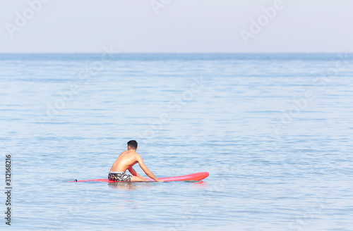 Handsome guy sitting on a surfboard in the sea