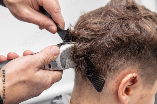 The hairdresser cuts the hair of a boy with a machine