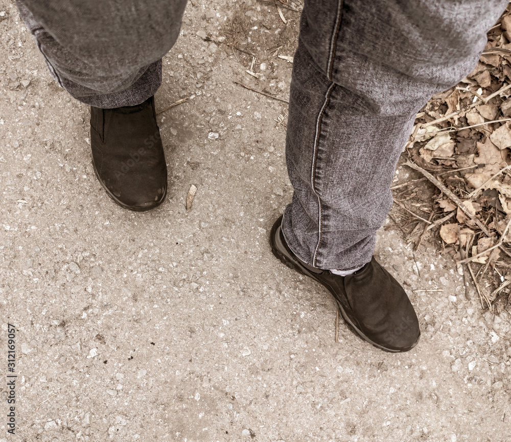 The legs of a man in jeans and shoes are on the road