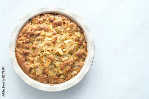 Homemade baked apple cake in a white round ceramic baking dish on a white background, top view