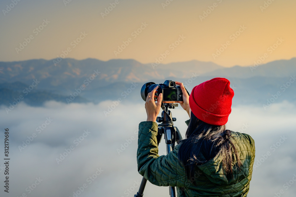 young woman traveller, photographer in the top peak of mountain in jungle forest alone, enjoy taking nature photo of the mist and flowing of foggy, northern part of Thailand travel