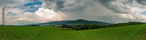panorama of landscape with hills, trees and green fields and storm clouds © Petr