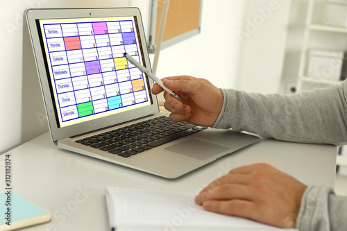 Young man using calendar app on laptop in office, closeup