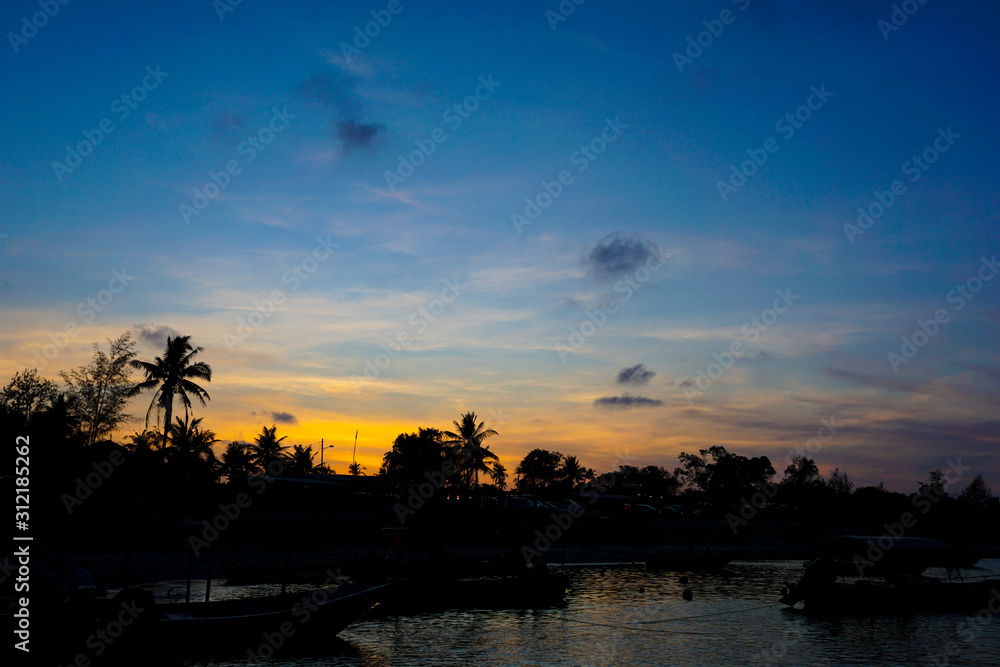 Silhouette of boat and fisherman village in blue and orange sunset background,soft focus
