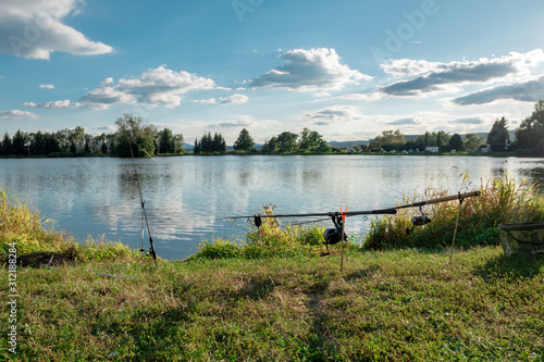 Beautiful fish pond in Badin, near Banska Bystrica, Slovakia. Sky reflection in the water. Fishing place. Shining sun over the fish pond in sunny day. Fishing rods. Catching fish. photo