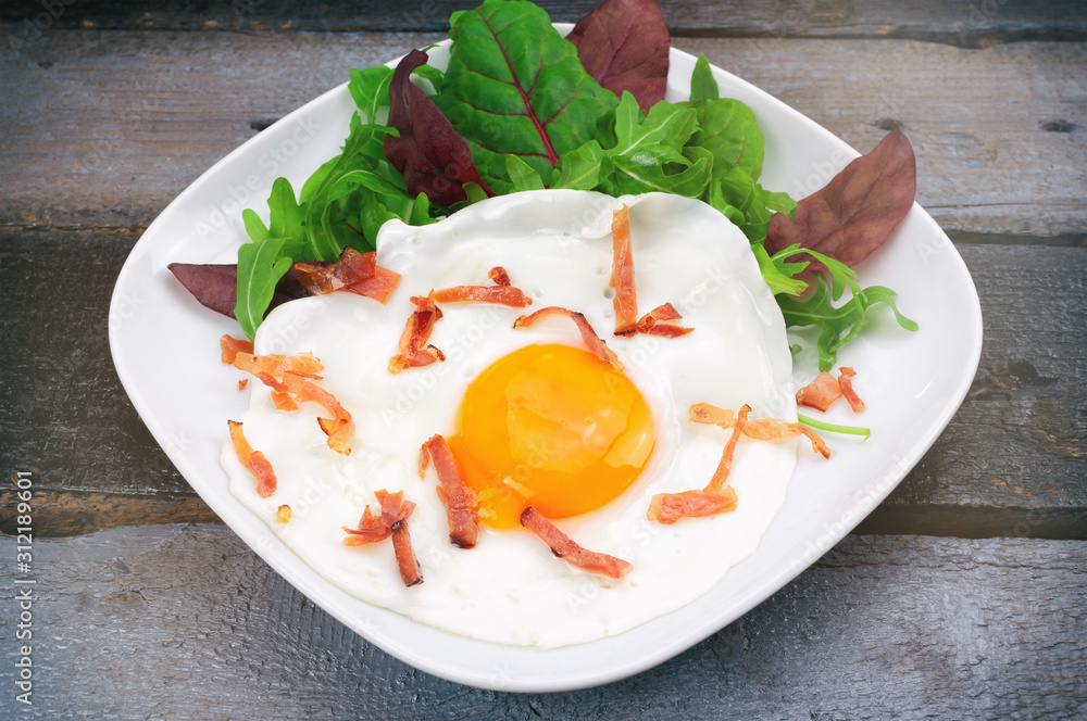 Fried egg with bacon and mixed salad on wooden table.