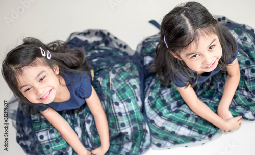 Identical twin girls sisters are posing for the camera. Happy twin sisters in dresses are looking at the camera and smiling. Frontal view, on white background
