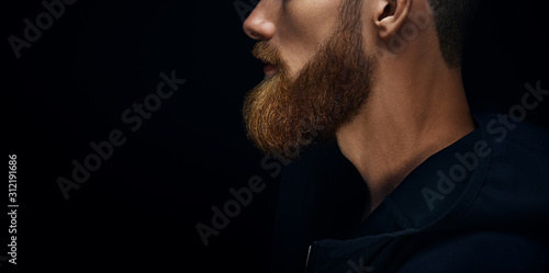 Single standing in profile young handsome serious bearded man in dark hoodie