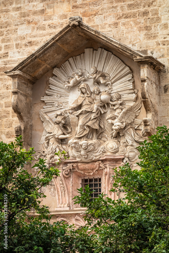Typical historical facade of Valencia old town with beautiful statue on the background and green trees at the front.