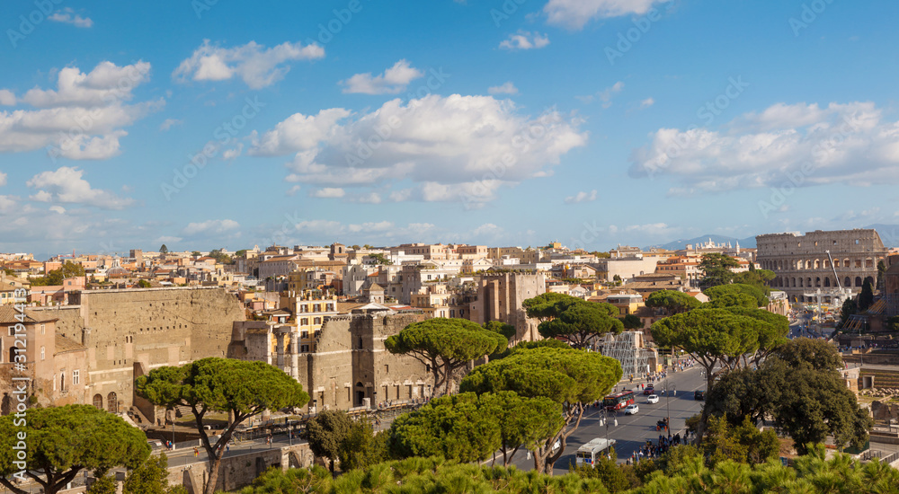 Horizontal panoramic view of the landscape of Rome with a view of the Colosseum, the road with cars, ancient ruins, green pine trees, blue sky with large clouds. Aerial view, Italy