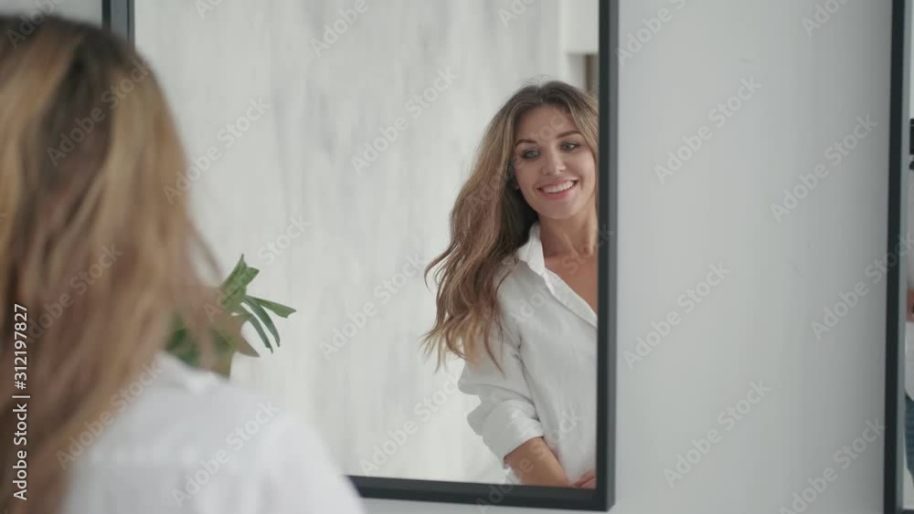 portrait of an attractive girl who admires herself in the mirror. young woman straightens her hair looking in the mirror portrait of an attractive girl who admires herself in the mirror. young woman straightens her hair looking in the mirror