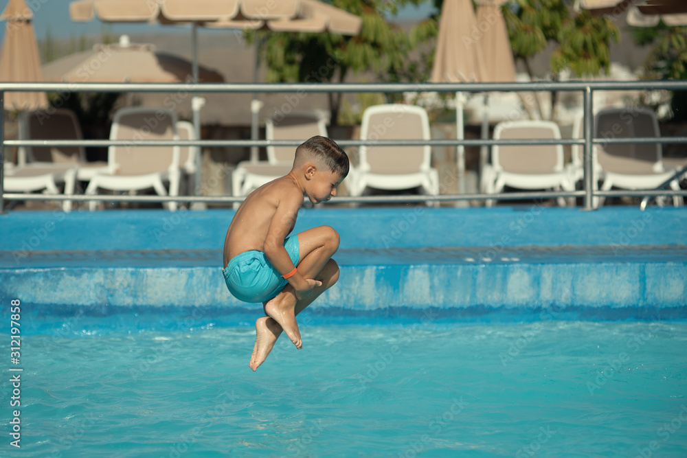 Caucasian boy having fun running to make jump into swimming pool at resort.  He is enjoying his summer vacations.