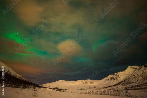 Dramatic polar lights  Aurora borealis with many clouds and stars on the sky over the mountains in the North of Europe - Tromso  Norway.long shutter speed.