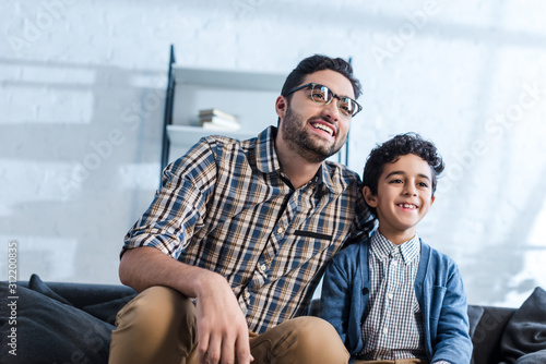 smiling jewish father and son watching tv in apartment