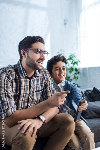 smiling jewish father pointing with finger and watching tv with son