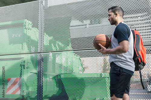 Fotografie Attractive basketball player walks beside a metal wall carrying his backpack and
