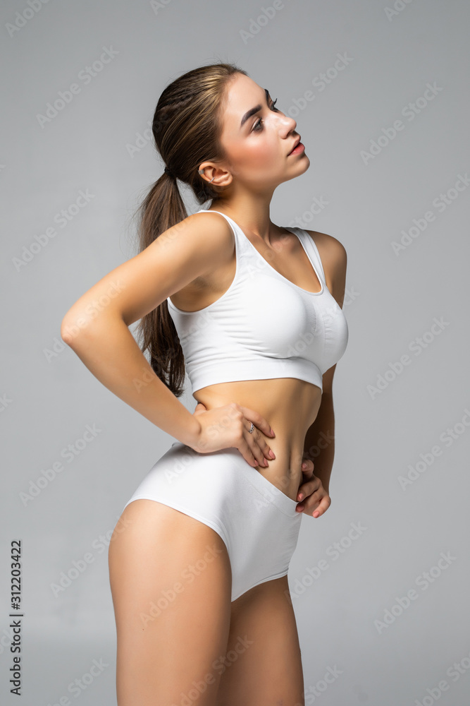 Slim tanned woman's body in white lingerie isolated over gray background Slim tanned woman's body in white lingerie isolated over gray background