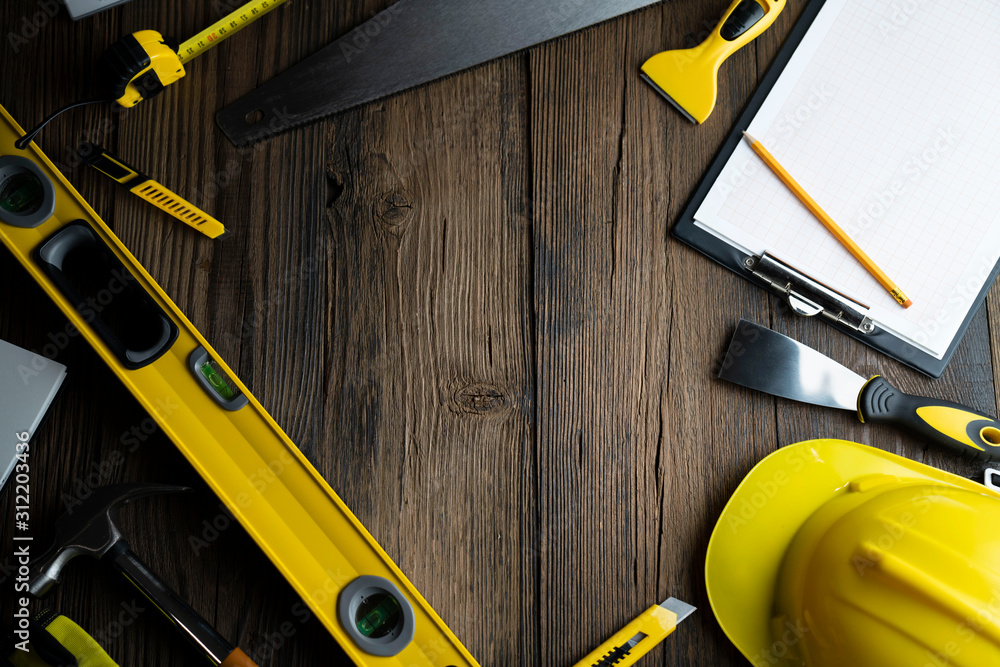 Contractor concept. Yellow hardhat, libella and other tools on the rustic wooden background.