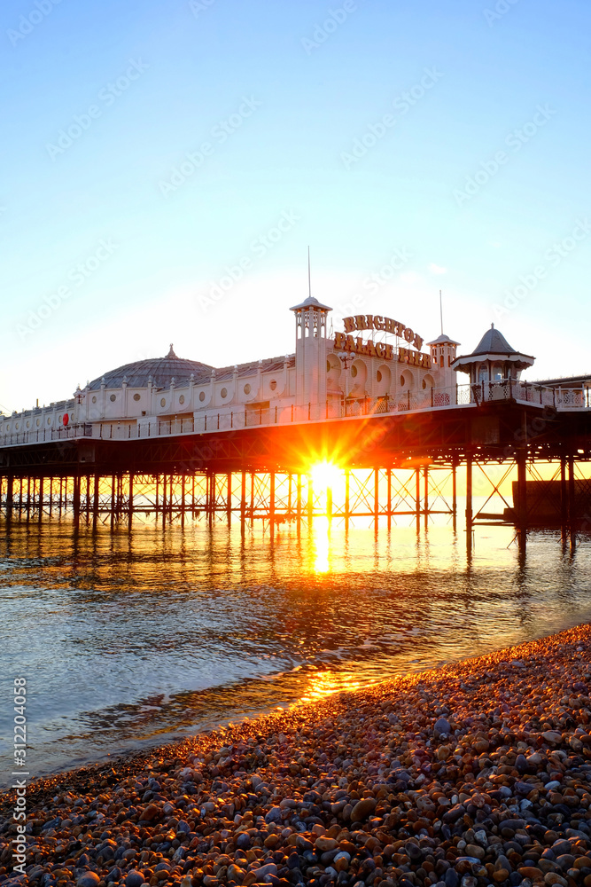 Obraz premium Brighton Palace Pier glowing yellow with the sun setting underneath it reflecting on a calm sea