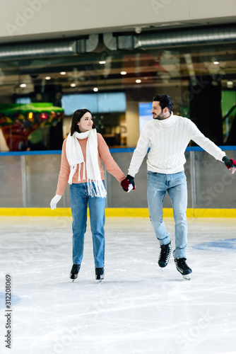 beautiful young couple in sweaters skating on rink