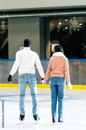 back view of young couple holding hands on skating rink
