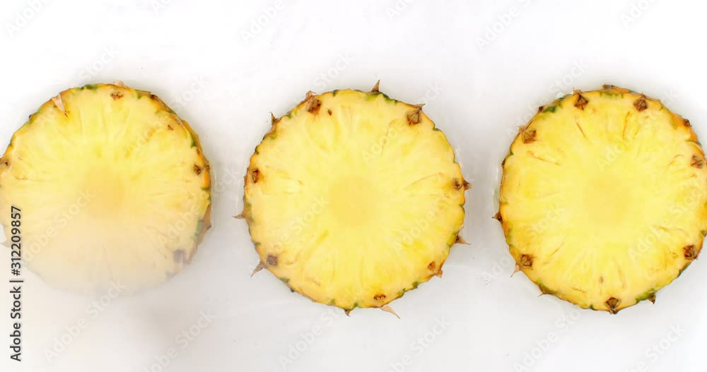 Top view: 3 slices of pineapple washed with water on a white background. Water splashes in slow motion Top view: 3 slices of pineapple washed with water on a white background. Water splashes in slow motion