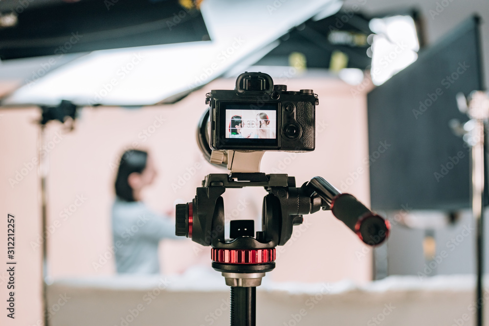 Selective focus of female model and assistant reflecting in camera display in photo studio