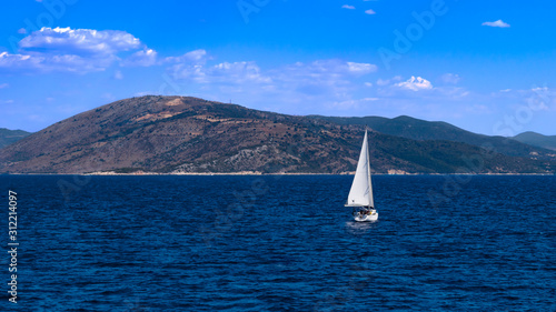 Picturesque sea landscape. The sea is a classic blue color and white sailing yacht on it. Mountains and sky in the background. View from the port of Lefkimmi. Corfu island, Greece. Copy space