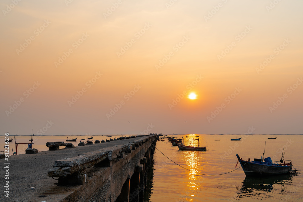 Beautiful seascape sunset with silhouette fishing wood boat floating down on sea at jetty in asia