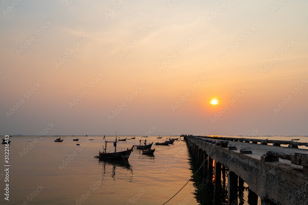 Fototapeta premium Beautiful seascape sunset with silhouette fishing wood boat floating down on sea at jetty in asia