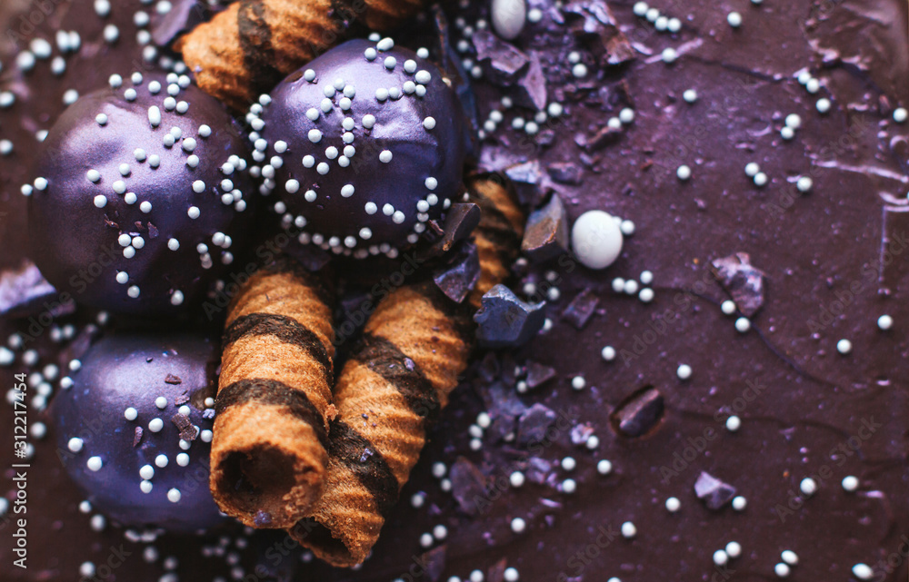 The surface of a blueberry cake with shiny purple chocolate icing. Homemade chocolate cake with blueberries and striped wafer rolls. The surface of a blueberry cake with shiny purple chocolate icing. Homemade chocolate cake with blueberries and striped wafer rolls.